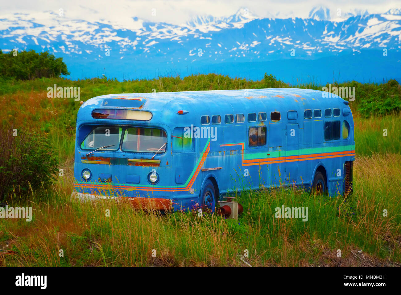 Kenai Mountain range is the backdrop of this old abandoned bus in a grassy field seen from walking path in Homer, Alaska. Stock Photo