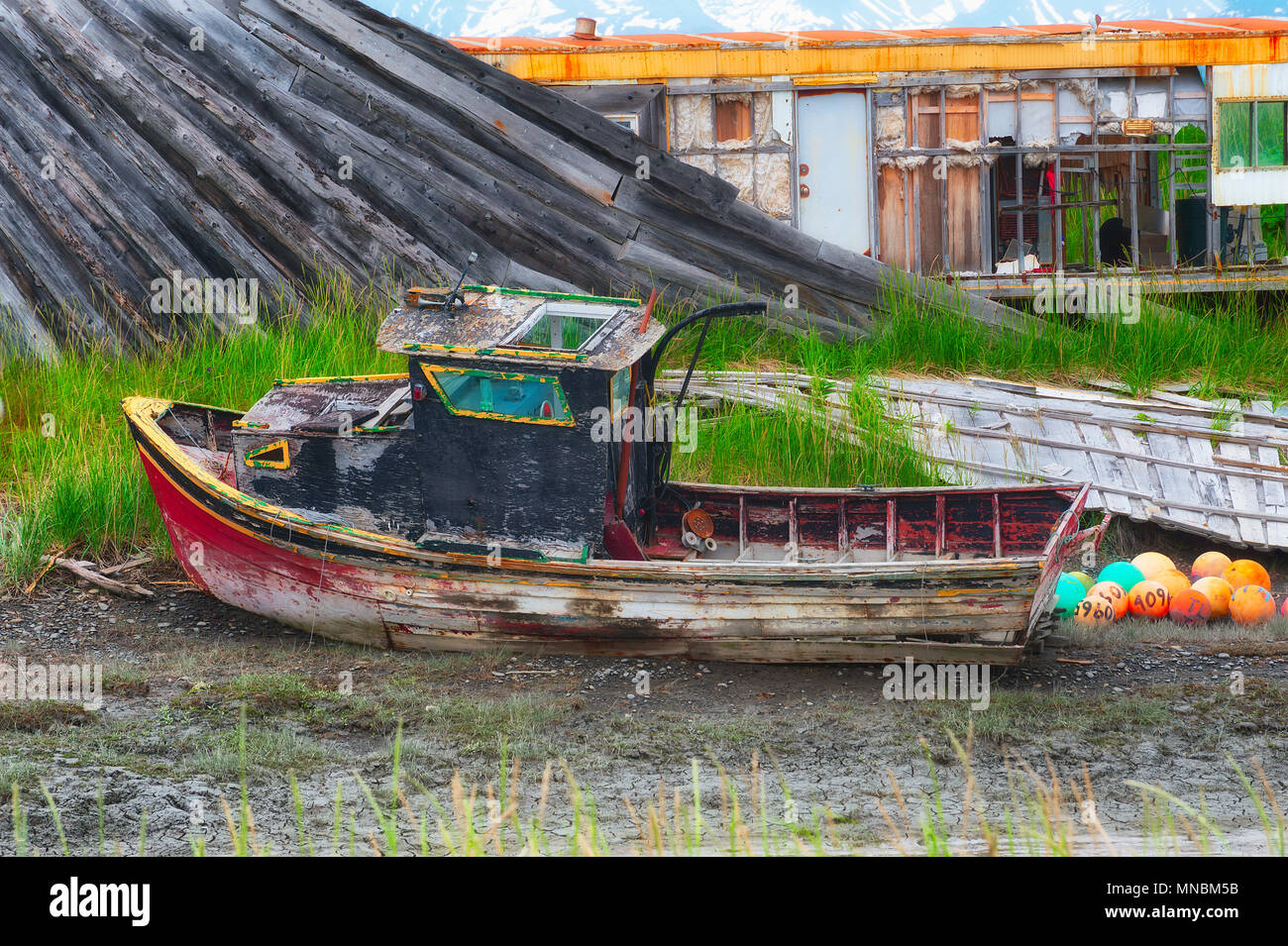 A rotting abandoned boat sits in a muddy grassy field among other decaying junk seen from the walking path along Kachemak Bay in Homer Alaska. Stock Photo