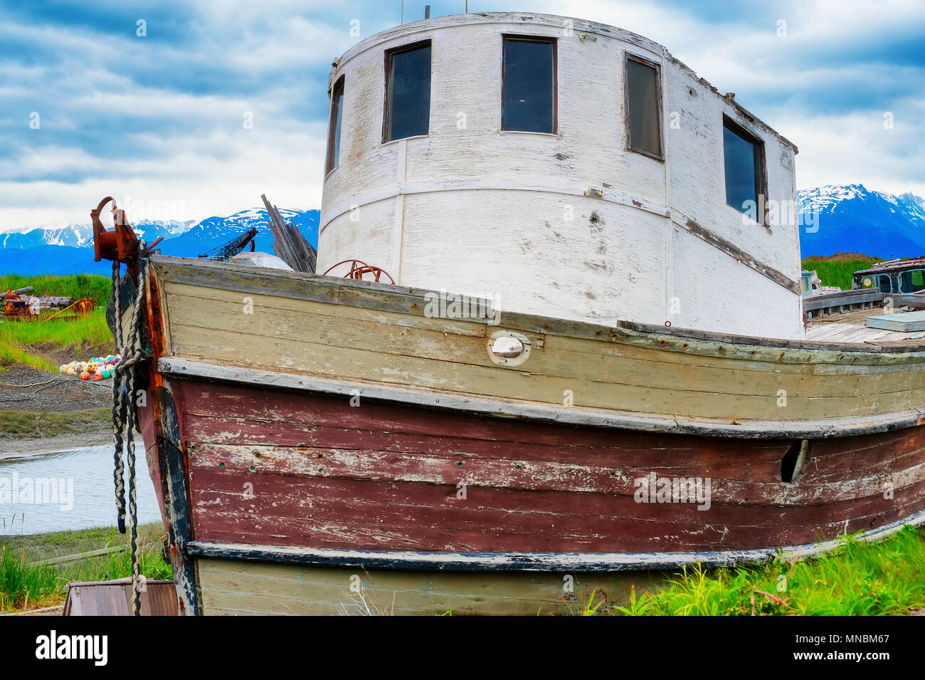 Decaying abandonded boat in a grassy field seen from walking path along the shores of Kachemak Bay in Homer Alaska. Stock Photo