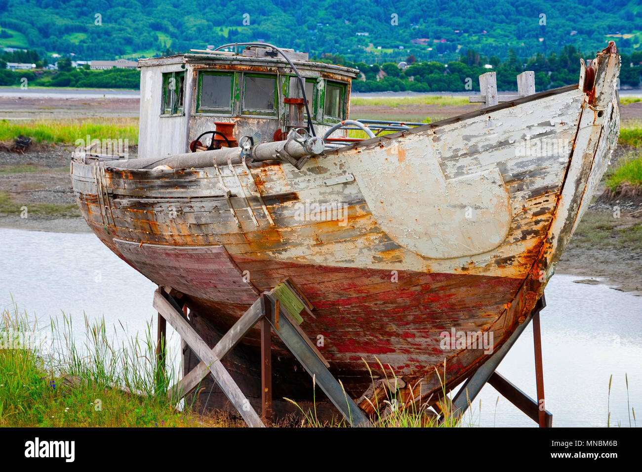 Decaying abandonded boat, sitting on a dry dock rack, in a grassy field seen from walking path along the shores of Kachemak Bay in Homer Alaska. Stock Photo