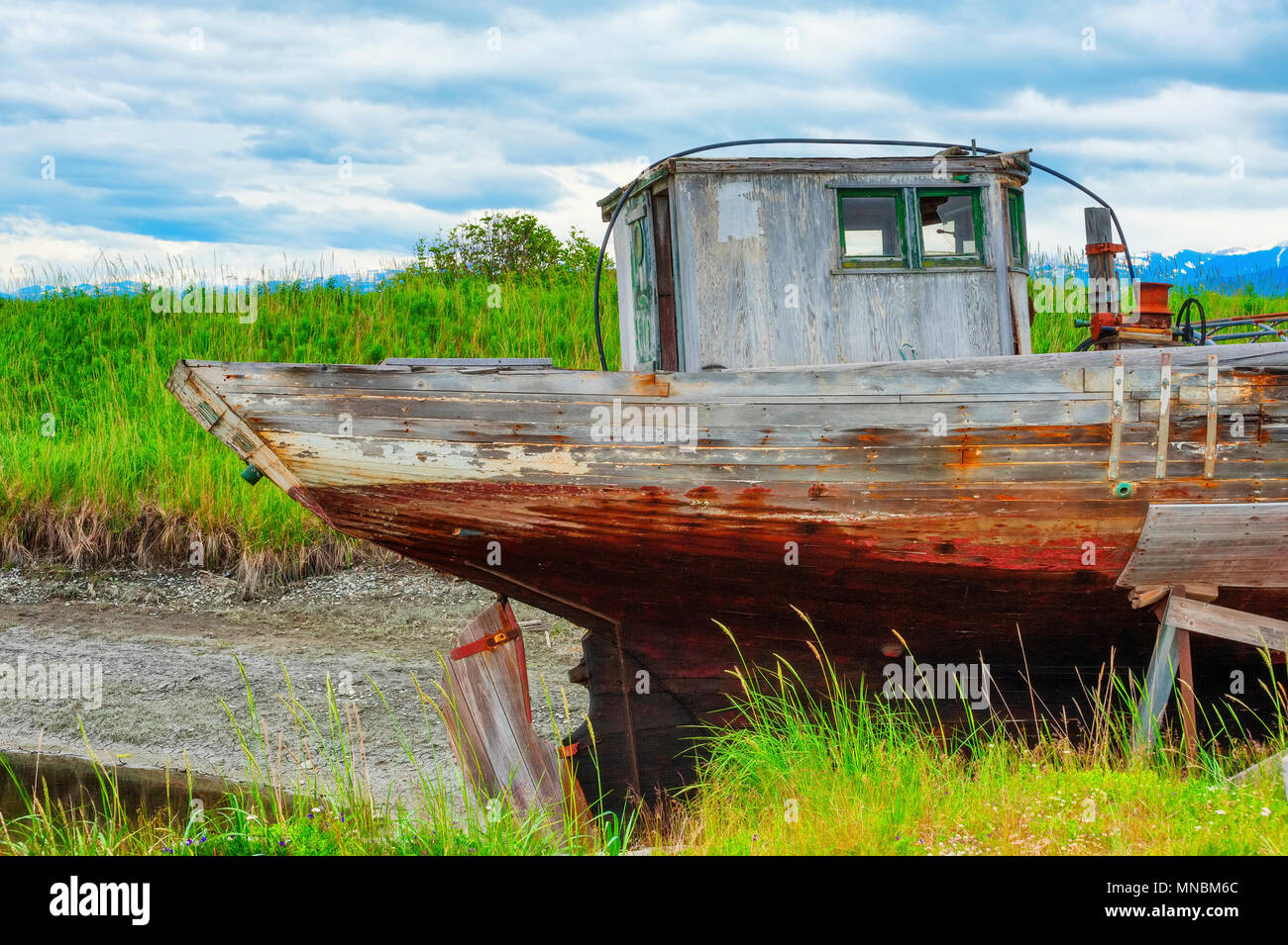 Decaying abandonded boat sitting in a dry dock rack in a grassy field seen from walking path along the shores of Kachemak Bay in Homer Alaska. Stock Photo