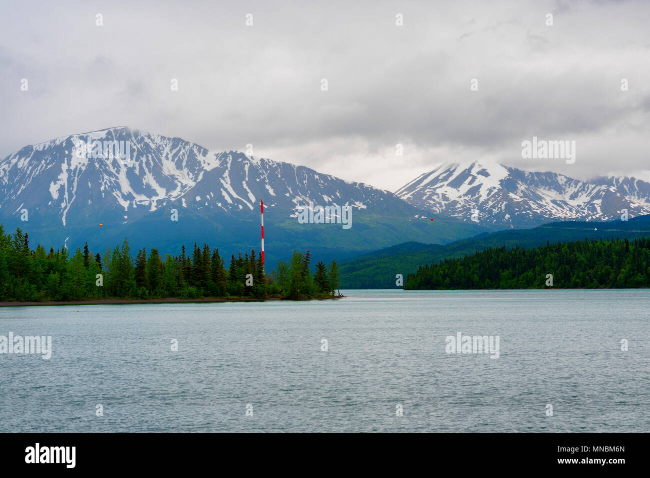 Lake Kenai under cloudy skies on a summer day where snow still can be seen in the distant mountain range. Stock Photo