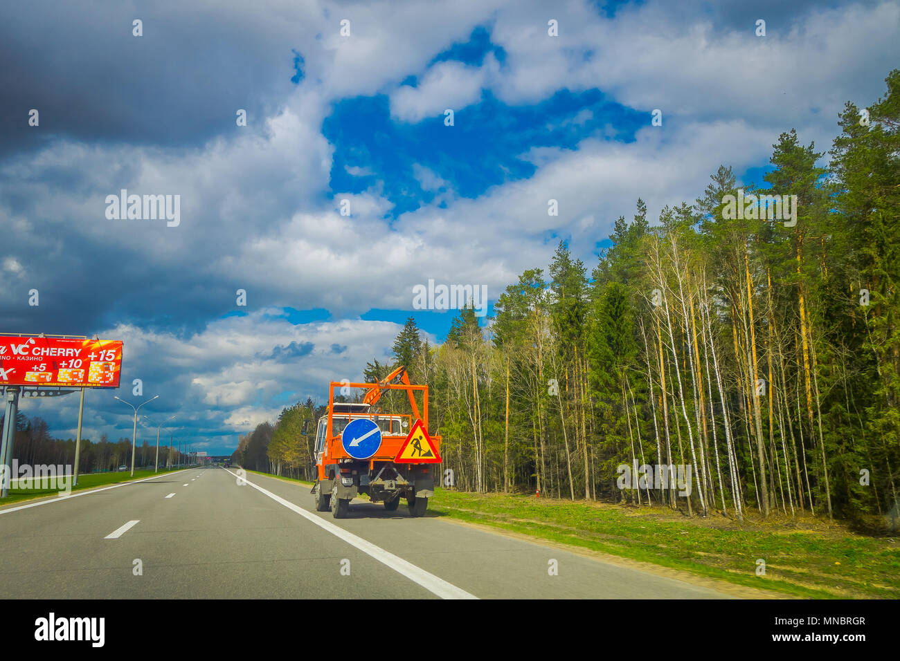 MINSK, BELARUS - MAY 01, 2018: Ooutdoor view of heavy machinery in the highway to the airport of Minsk against dramatic clouds background with trees at each side of the road Stock Photo