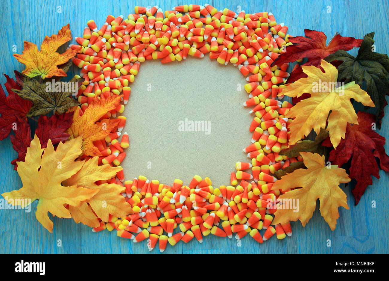 Frame of candy corns with fall leaves. Surrounding the edges of the frame is a green rustic wooden background.  Fall concept sale sign/ party invites. Stock Photo
