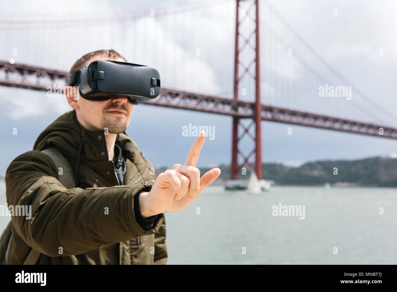 A man uses virtual reality glasses. 25th of April bridge in Lisbon in the background. The concept of virtual travel. The concept of modern technologies and their use in everyday life Stock Photo