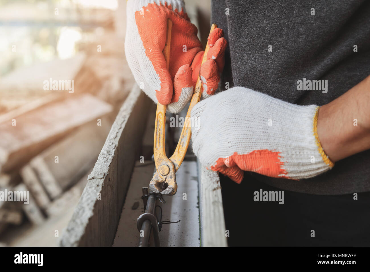 Close up of workers hands using pincers bind steel wire to rebar before