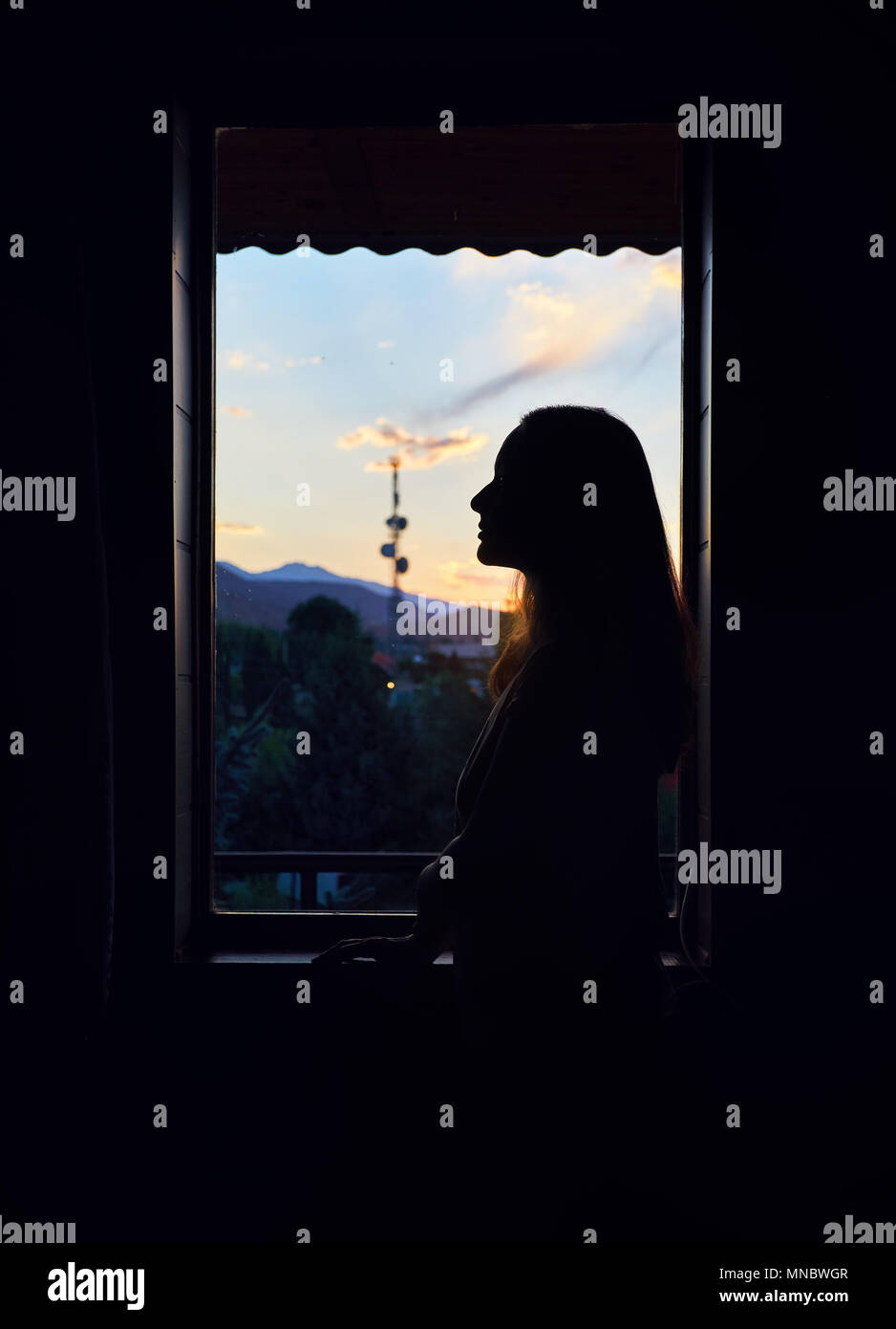 Silhouette of beautiful woman near the window at hotel with sunrise sky in Kyrgyzstan Stock Photo