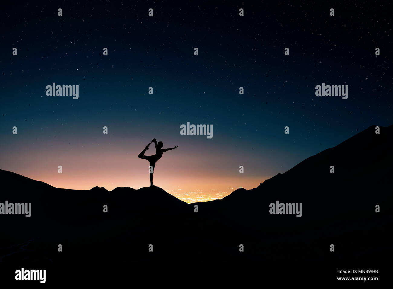 Fit Man in silhouette doing yoga natarajasana pose at night city and starry sky background Stock Photo
