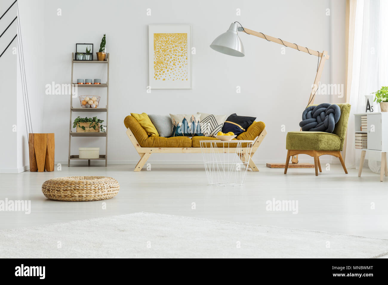 Mustard couch with colorful pillows standing under oversize lamp Stock