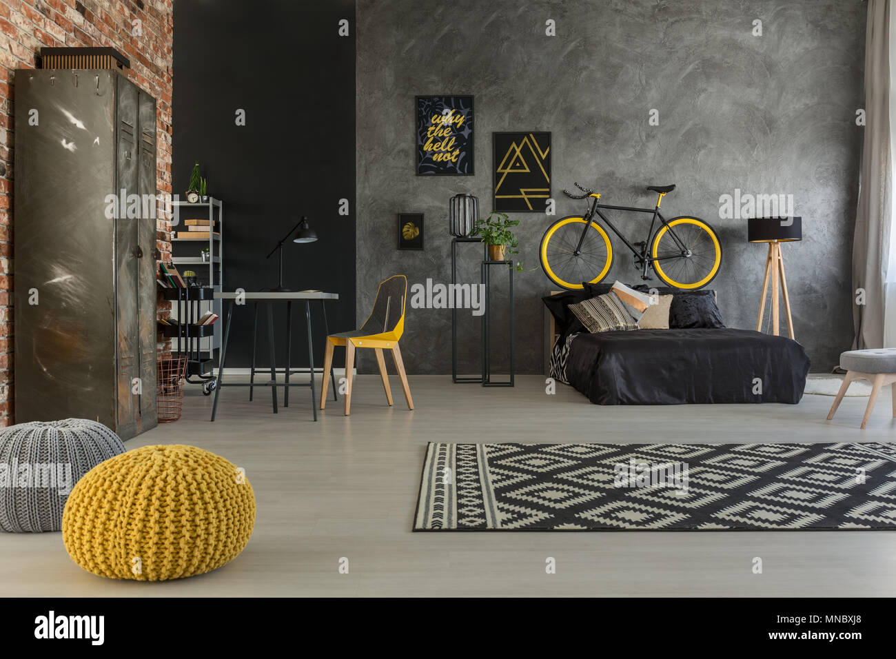 Grey apartment with bed, desk, chair, brick wall, yellow details Stock