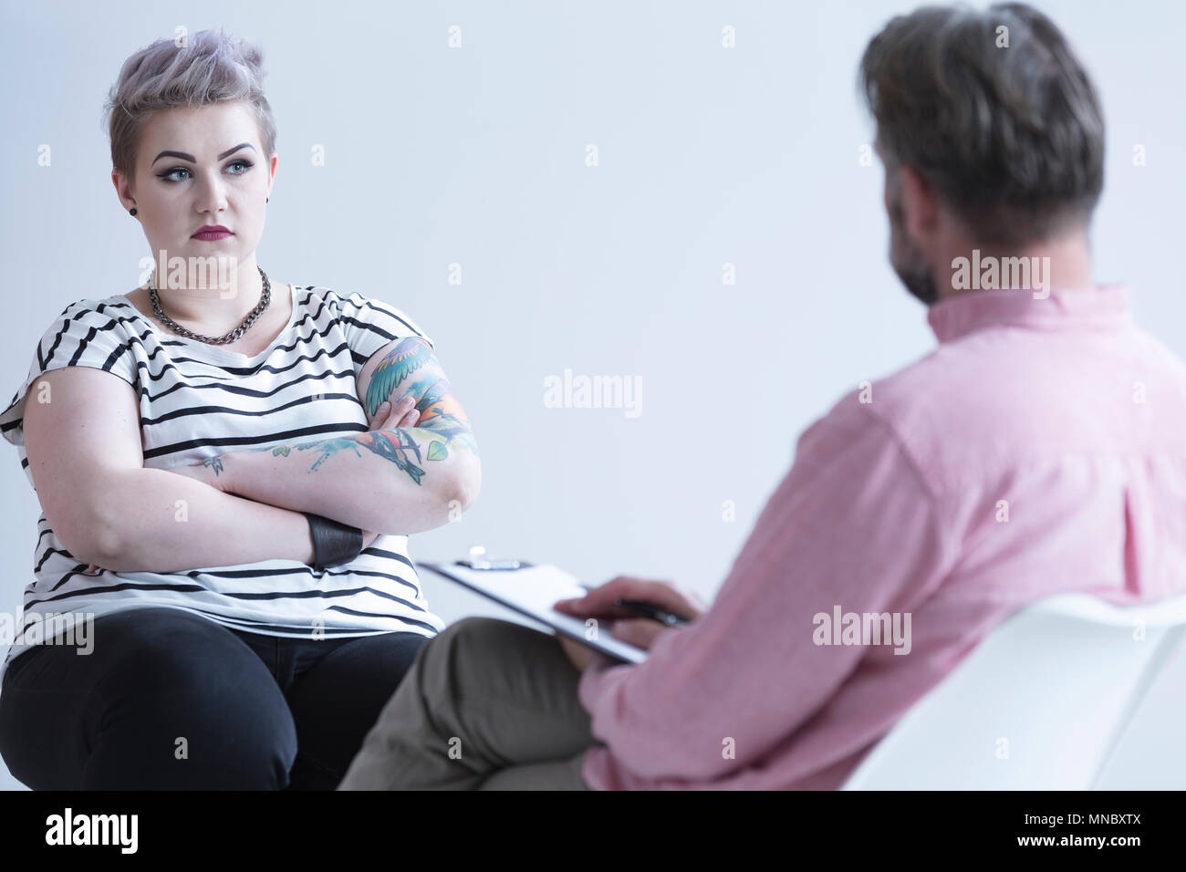 Troubled girl with tattoo and dark makeup talking with psychologist Stock Photo