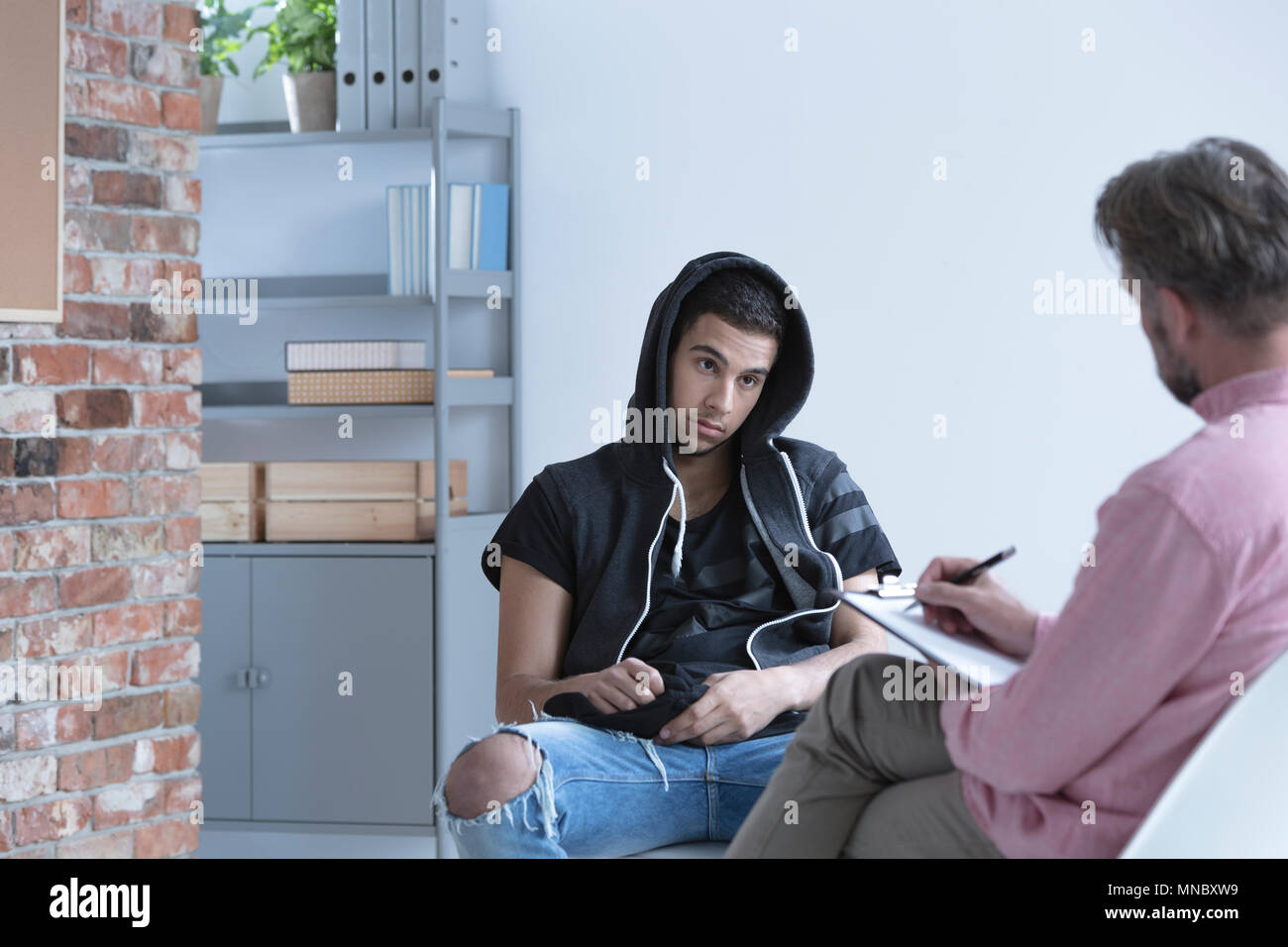 Rebellious boy with hood during session with psychotherapist Stock Photo