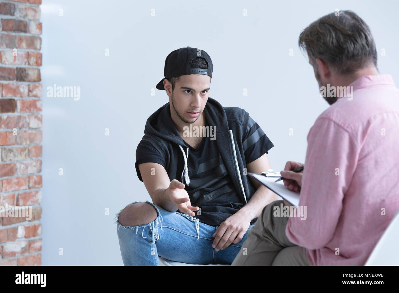 Teenage boy wearing cap, talking with his psychologist Stock Photo