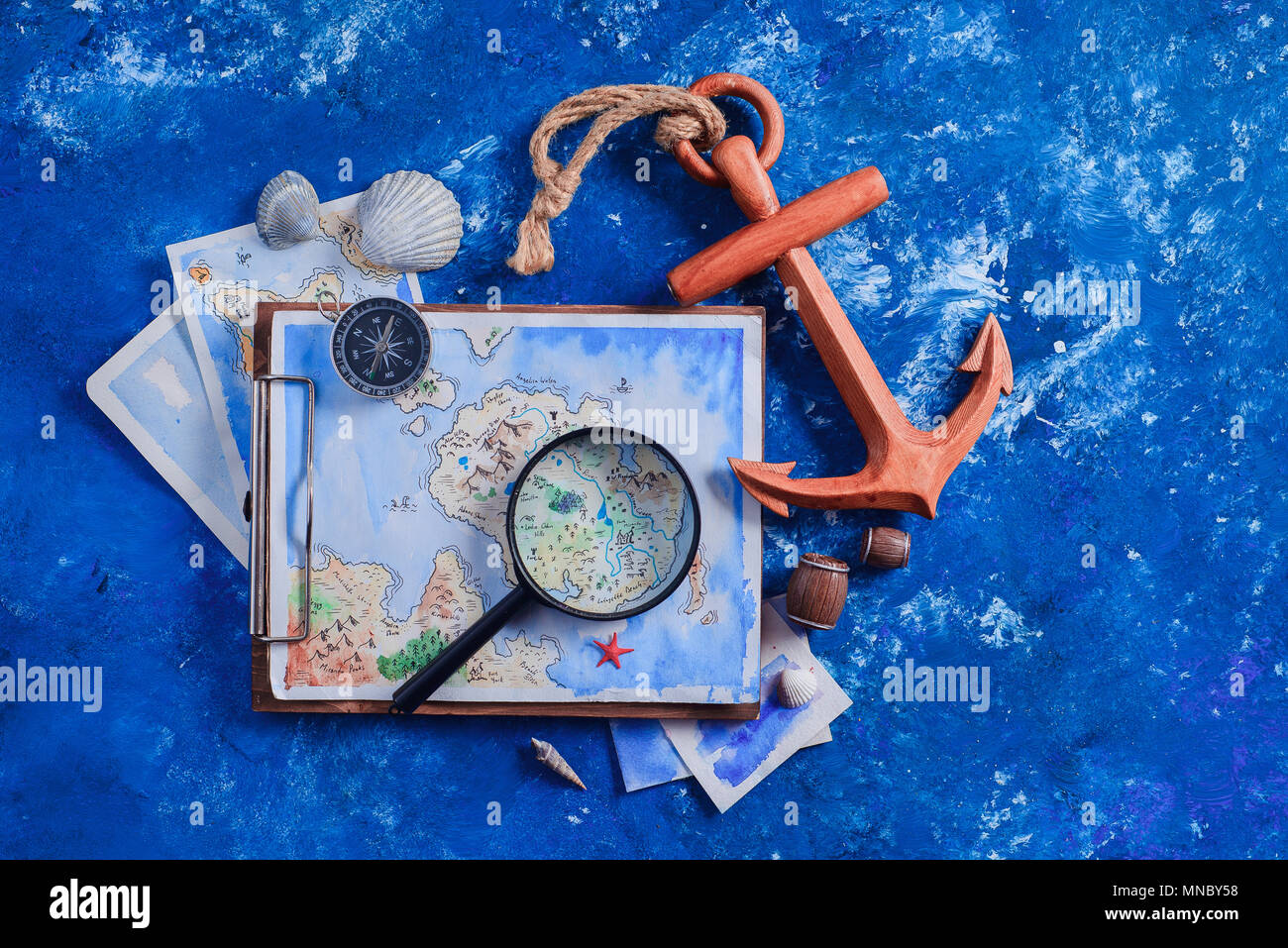 Travel flat lay with wooden anchor, fantasy map, watercolor sketches, seashells and compass on a navy blue background with copy space. Creative artist Stock Photo