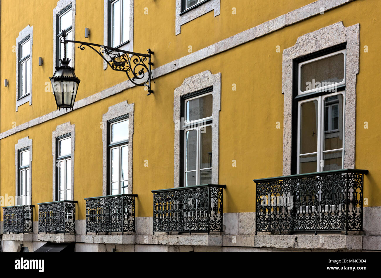 View along ochre coloured wall with ornate ornamental balconies, French windows and a wall-mounted street lamp Stock Photo