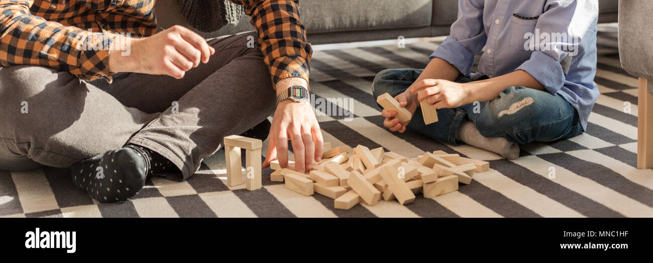 Close-up of man and kid arranging wooden bricks on a carpet at home Stock Photo
