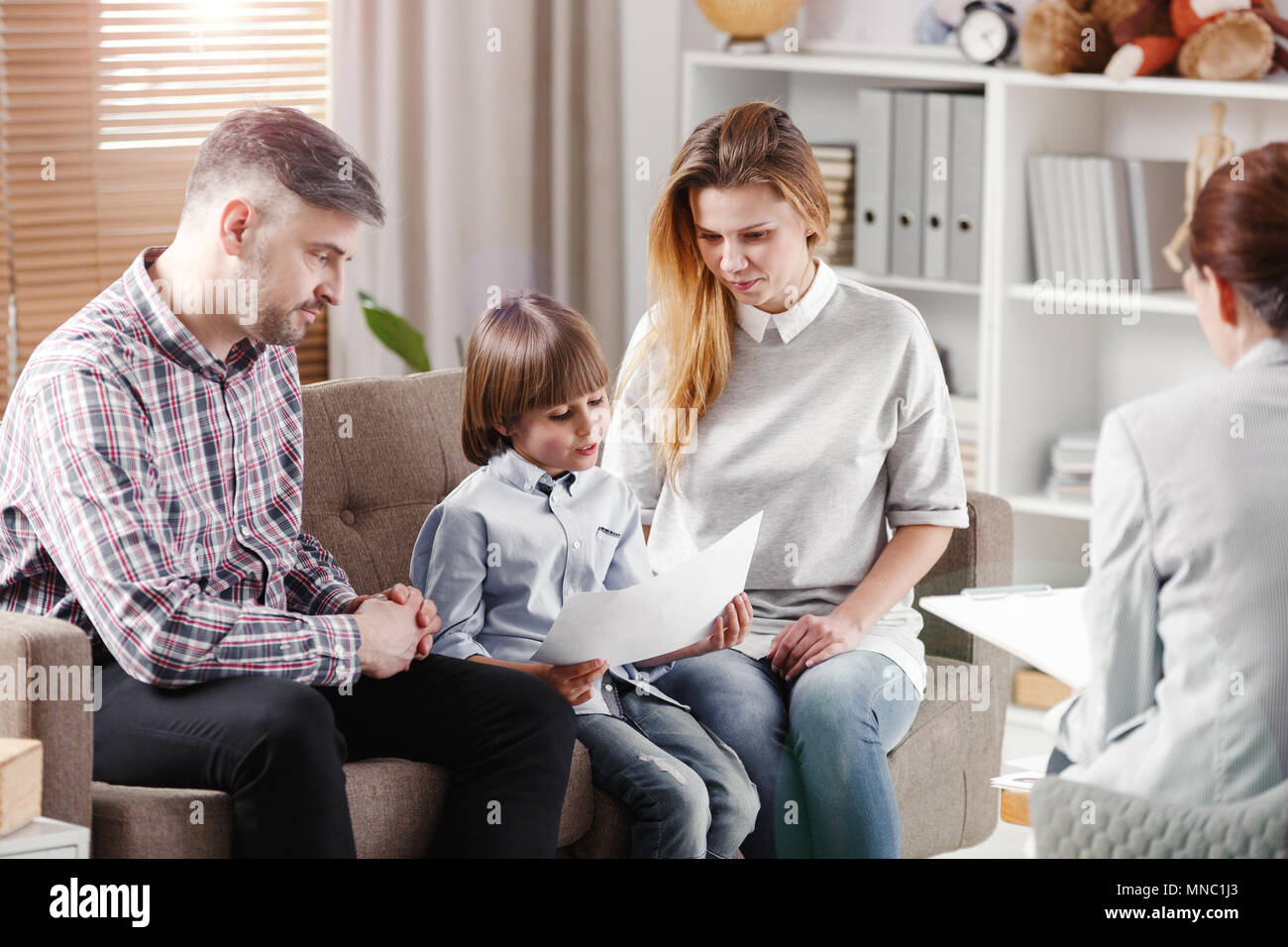 Autistic boy describing a picture while sitting with his parents during consultation with therapist Stock Photo