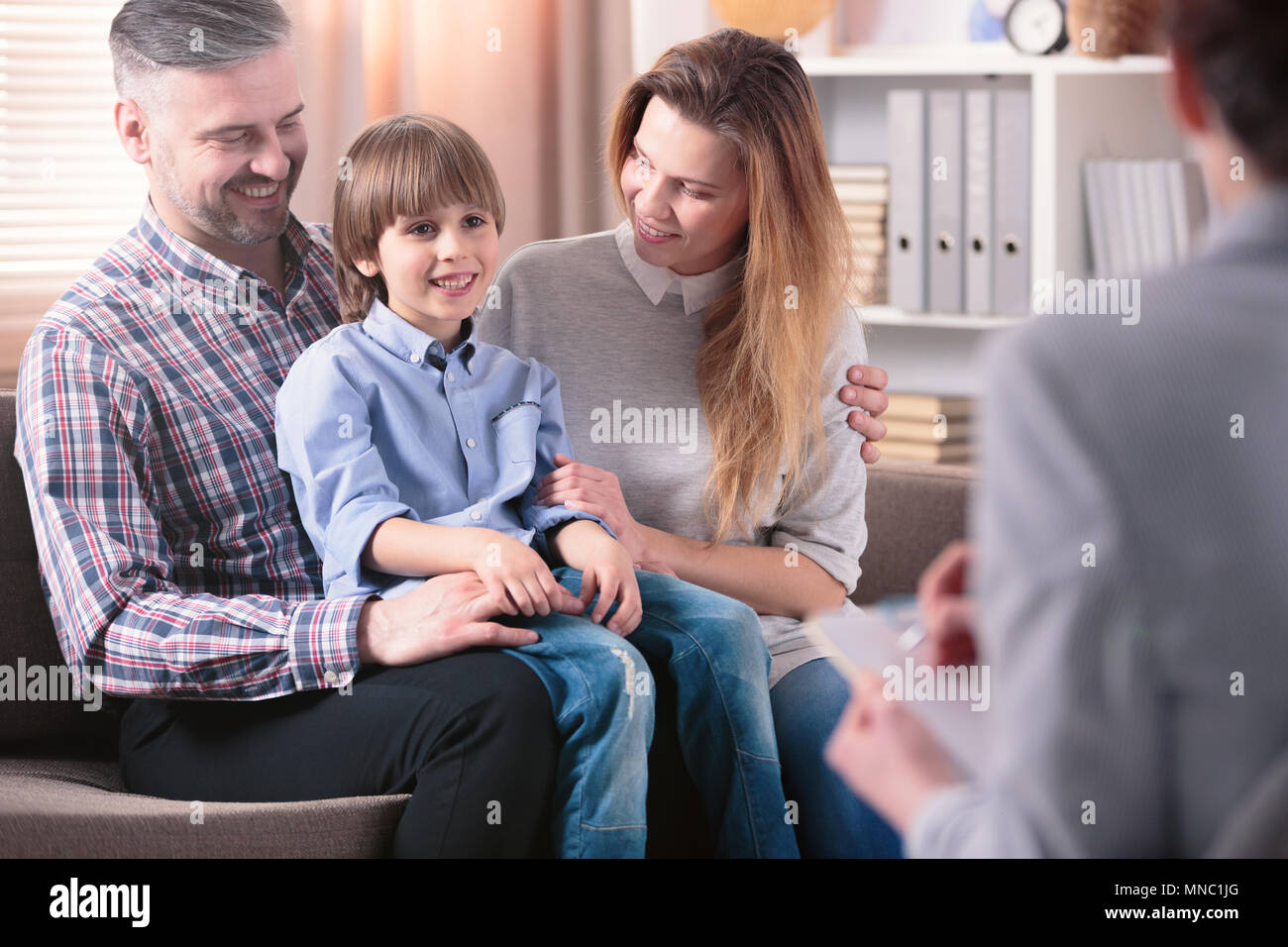 Happy kid sitting on his father's lap next to his mother during a meeting with school counselor Stock Photo