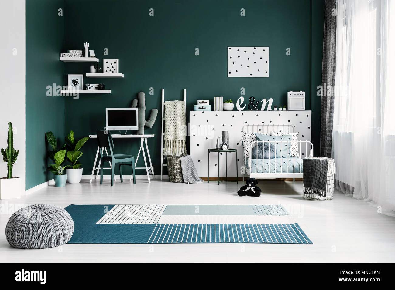 Grey pouf on blue carpet in spacious teenager's room interior with green chair at desk next to plants Stock Photo