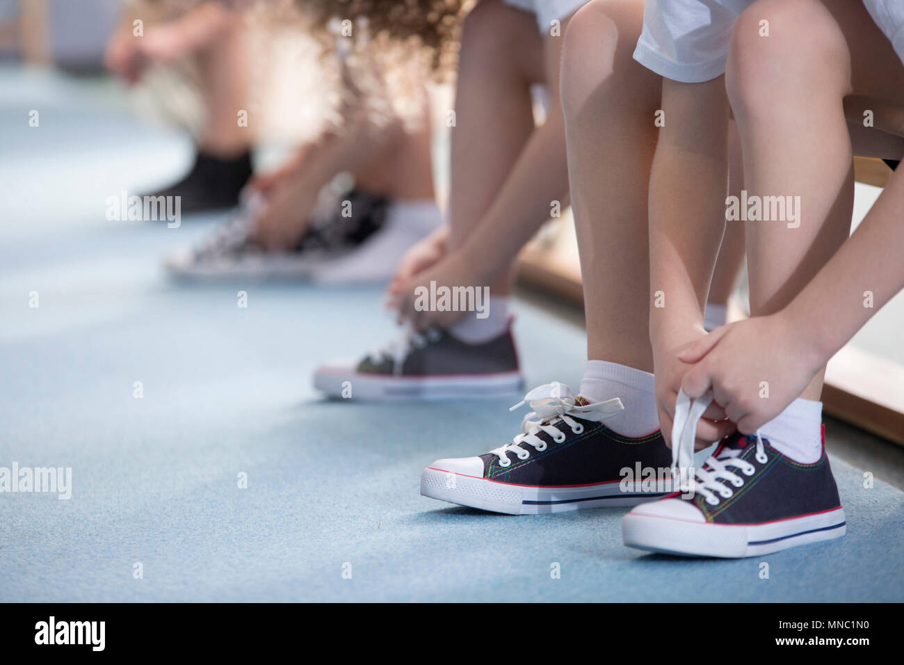 Close-up on school kids' legs while they're sitting on a bench and tying  their sport shoes for physical education activities Stock Photo - Alamy
