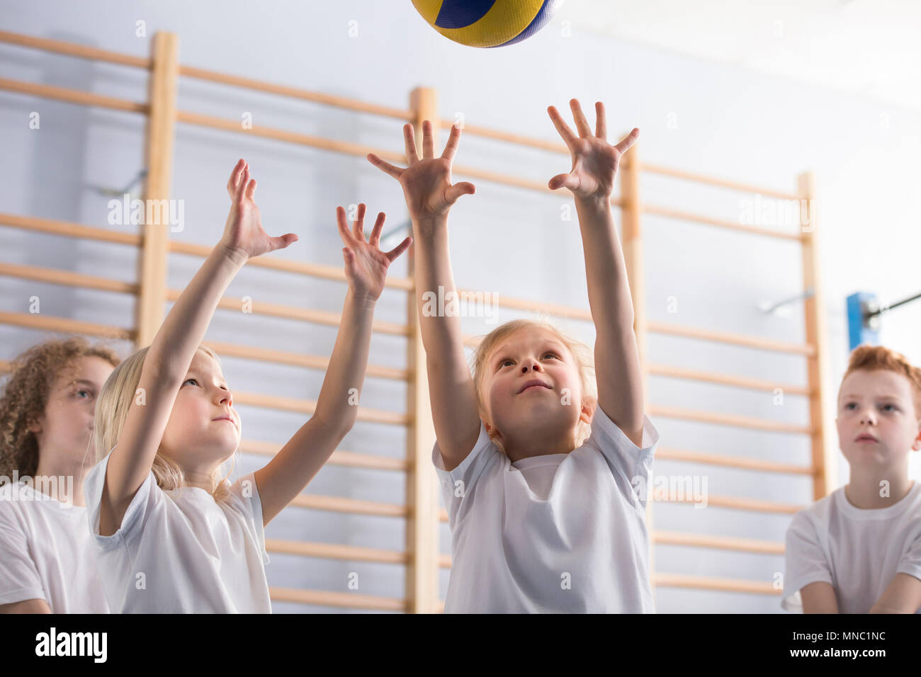 Young girl with her arms up jumping to hit a volleyball during a game with her school team mates at extracurricular physical education class in the gy Stock Photo