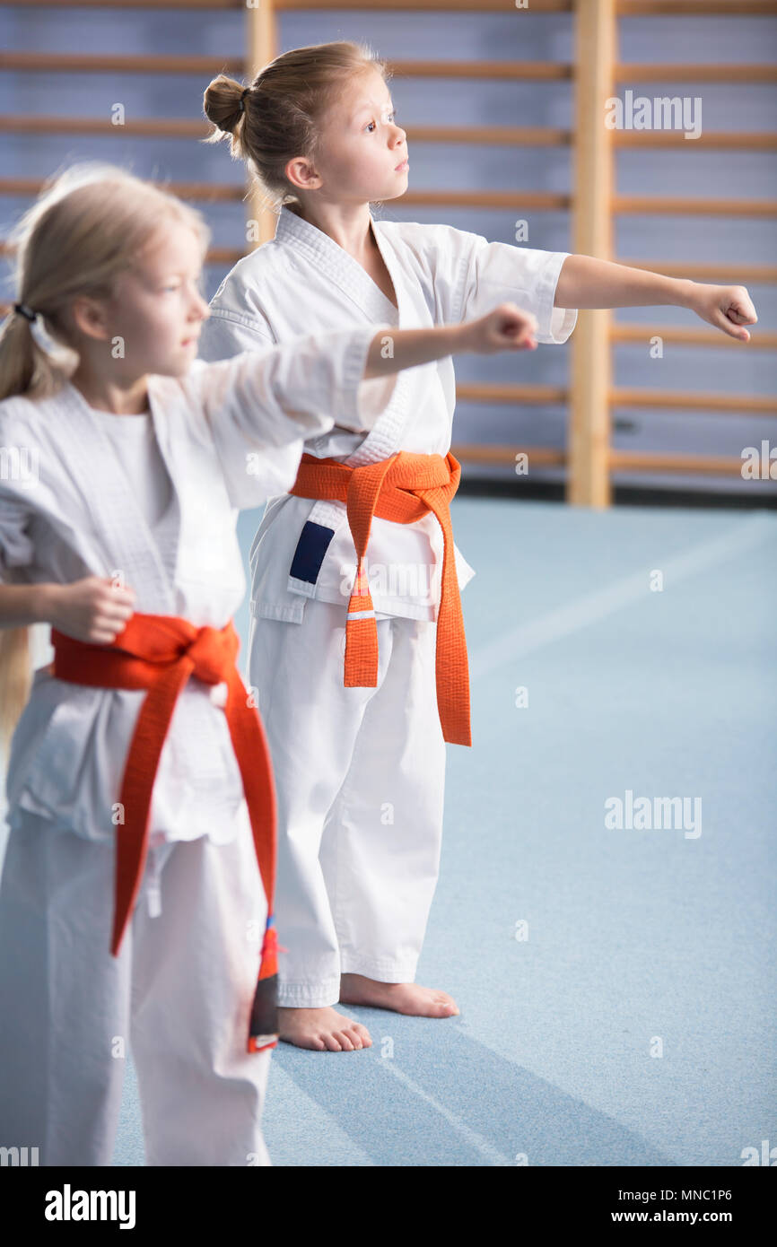 Young girls wearing orange belts, training moves and looking in the direction of their coach during karate classes Stock Photo