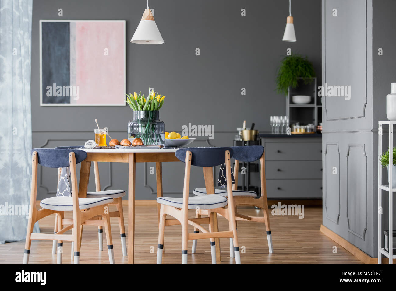 Grey dining room interior with pink and blue painting, wooden table and chest of drawers Stock Photo