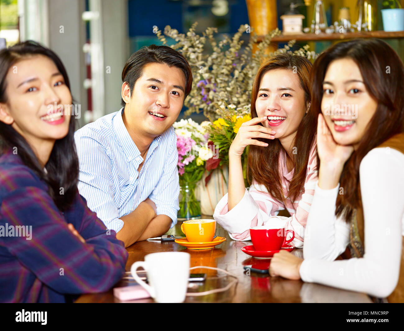 group of four happy asian young adults man and woman looking at camera smiling while gathering in coffee shop. Stock Photo