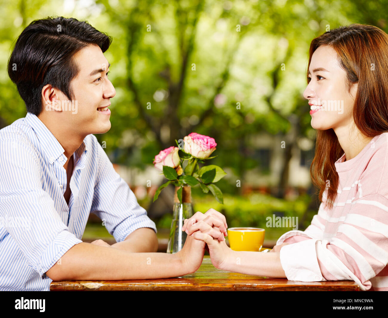 young asian man and woman sitting face to face holding hands looking at each other in coffee shop. Stock Photo