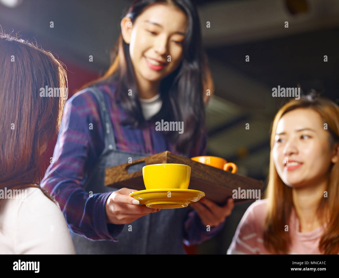 young smiling asian waitress serving coffee to customers, focus on the cup. Stock Photo