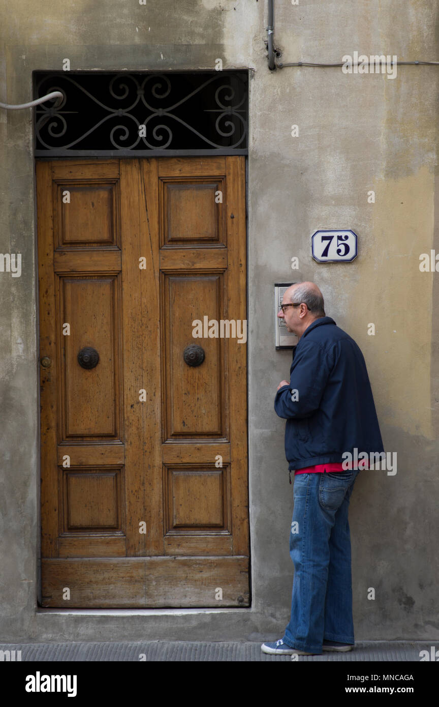 man listens at a door intercom after ringing the doorbell of number 75 in florence italy Stock Photo