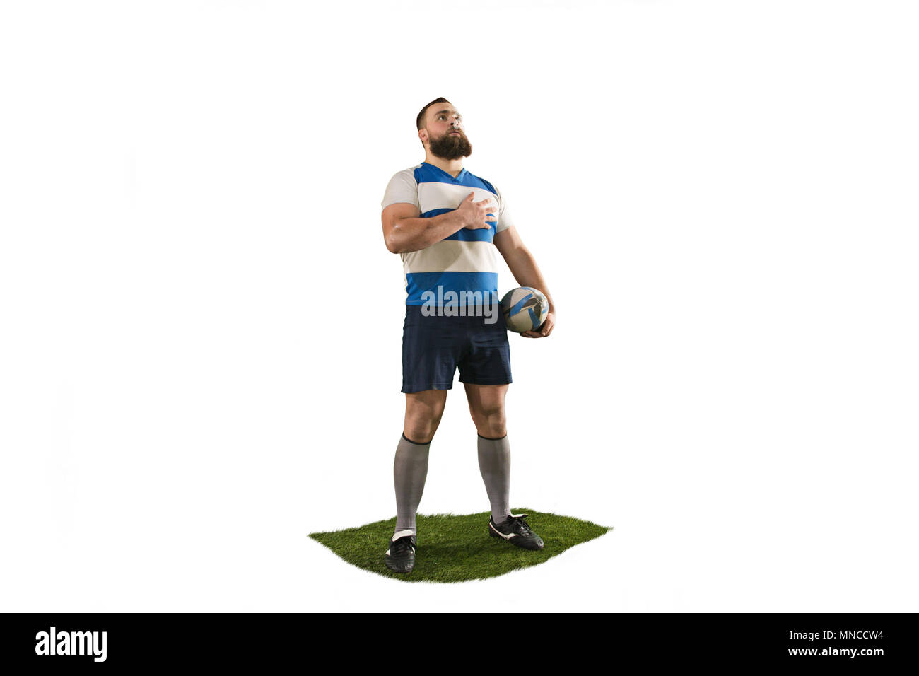 The silhouette of one caucasian rugby man player isolated on white background. Studio shot of fit man standing with ball and singing national anthem.  Stock Photo
