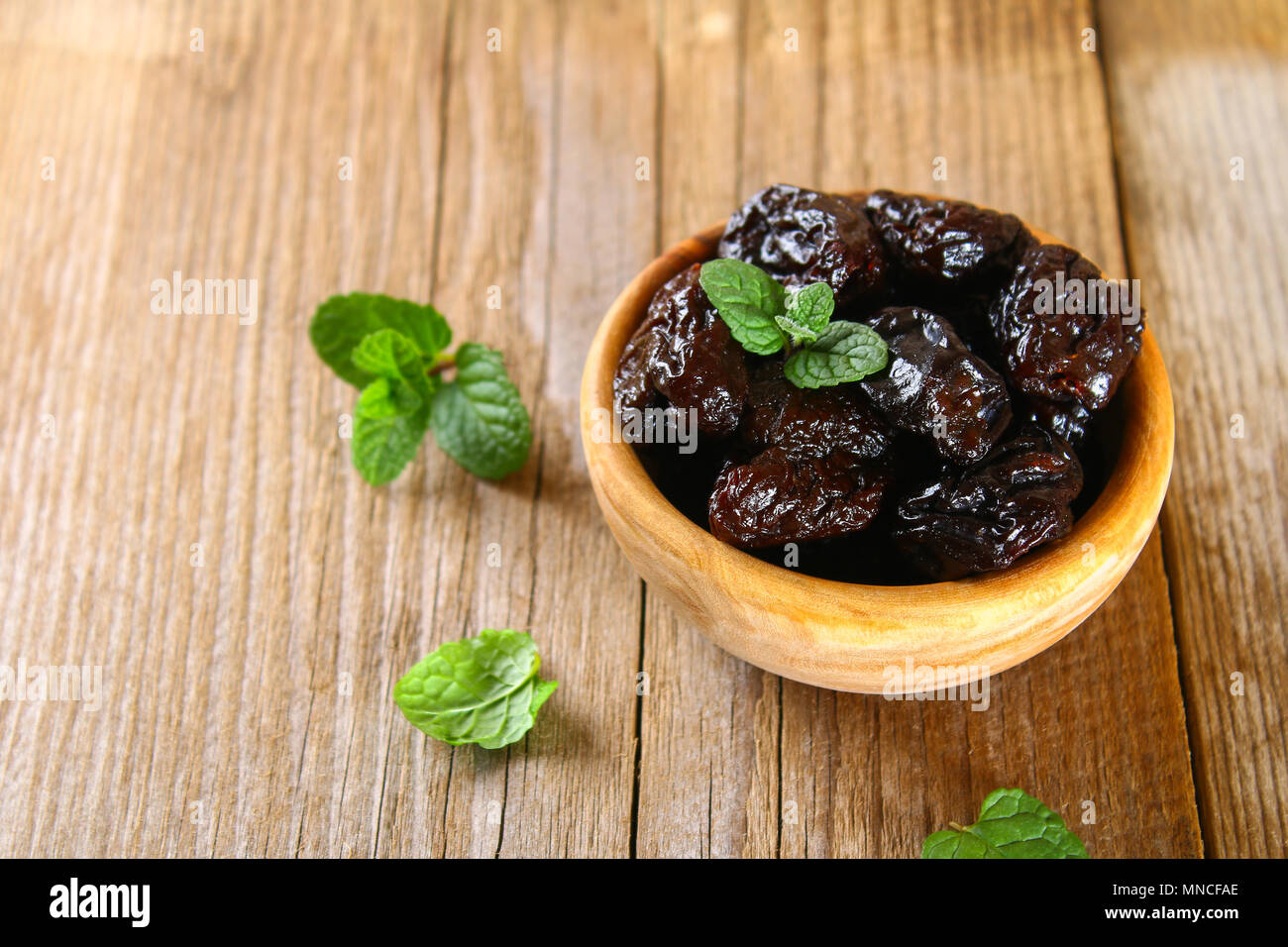 Prunes with mint leaves in a bowl on an old wooden table Stock Photo