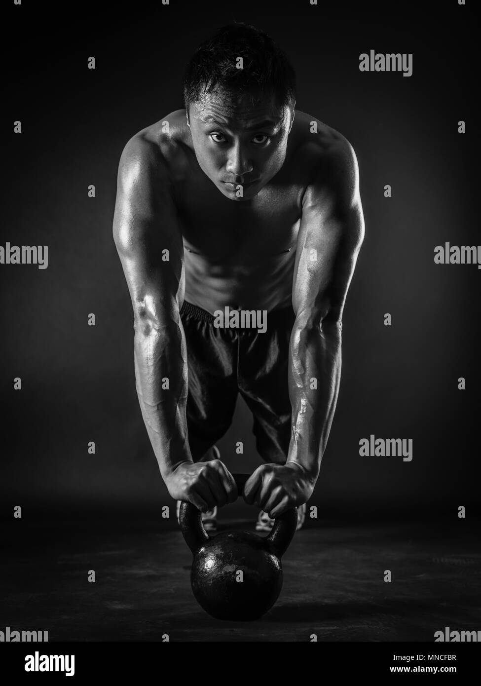 Photo of a muscular Asian man doing pushups with a kettlebell. Focus on his face. Stock Photo