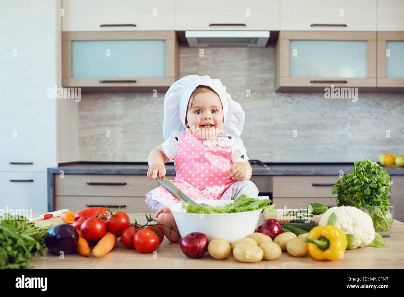 A little girl in a chefs hat prepares in the kitchen. Stock Photo
