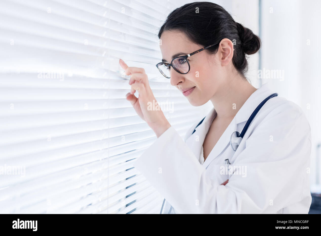 Young female physician smiling while looking through the window  Stock Photo