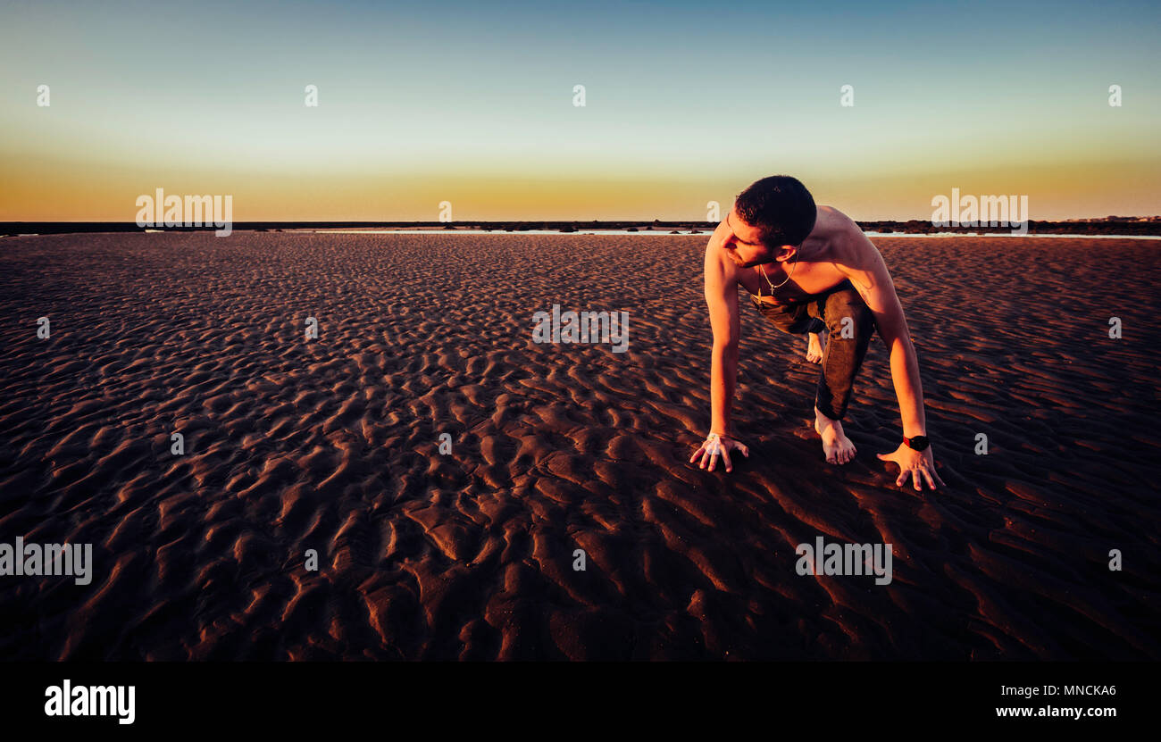 Young man doing yoga in the sand of the beach of Sanlucar de Barrameda at sunset, when the tide is low Stock Photo
