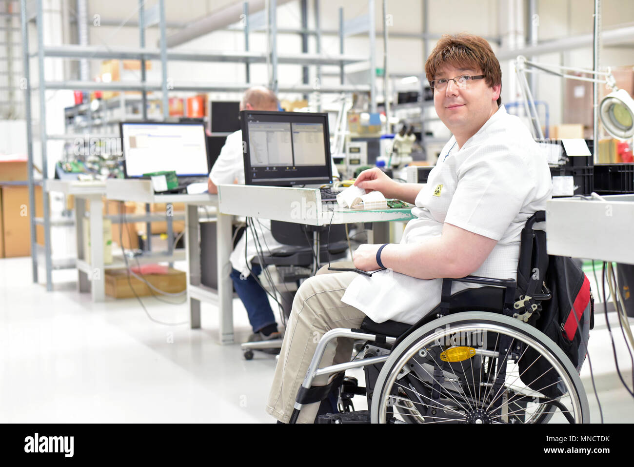handicapped worker in a wheelchair assembling electronic components in a modern factory at the workplace Stock Photo