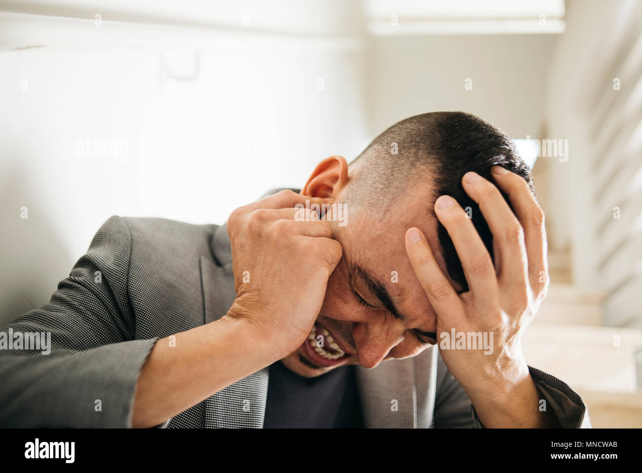 closeup of a suffering caucasian man with one hand in his head and the other hand covering his ear Stock Photo
