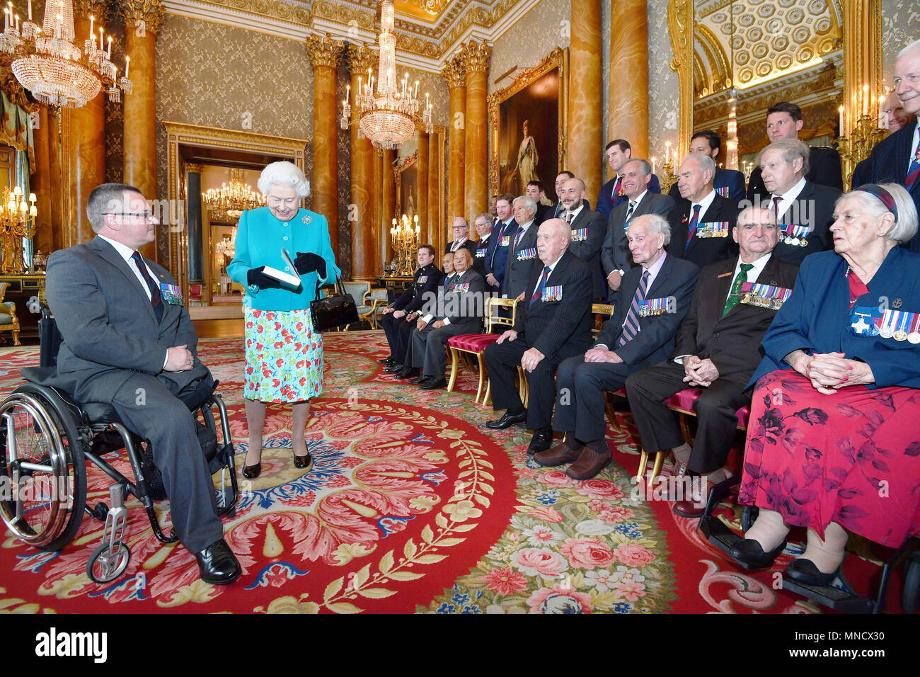 Queen Elizabeth II is given a book by Major Peter Norton GC (left), which recalls the exploits by the twenty-five living recipients of the Victoria and George Cross medals, following a group photograph taken at Buckingham Palace in London. Stock Photo