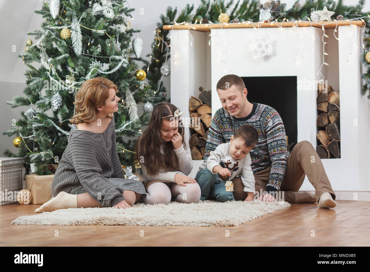 Happy family sitting on rug by Christmas tree at home Stock Photo