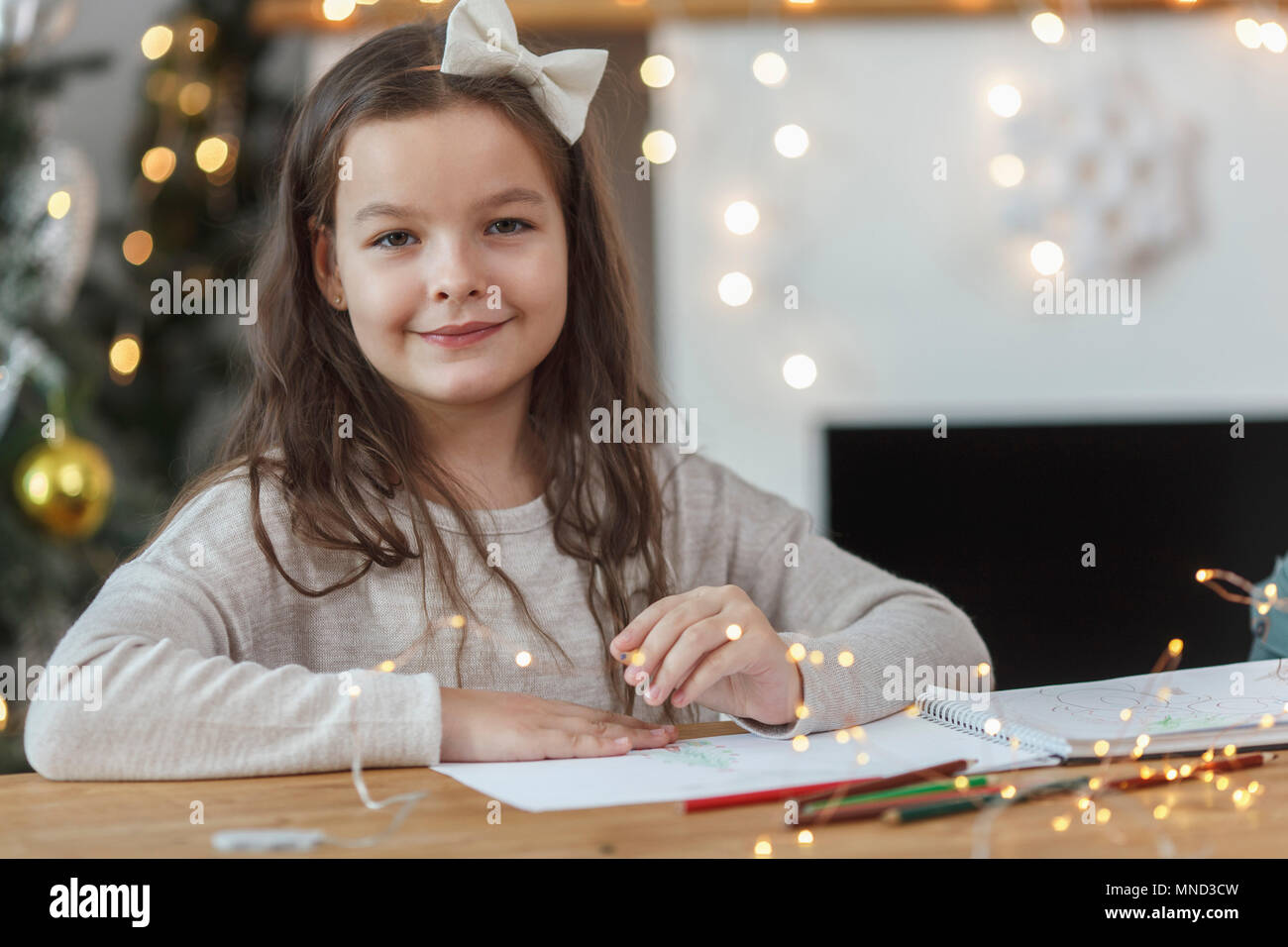 Portrait of smiling girl sitting at table with illuminated string lights Stock Photo
