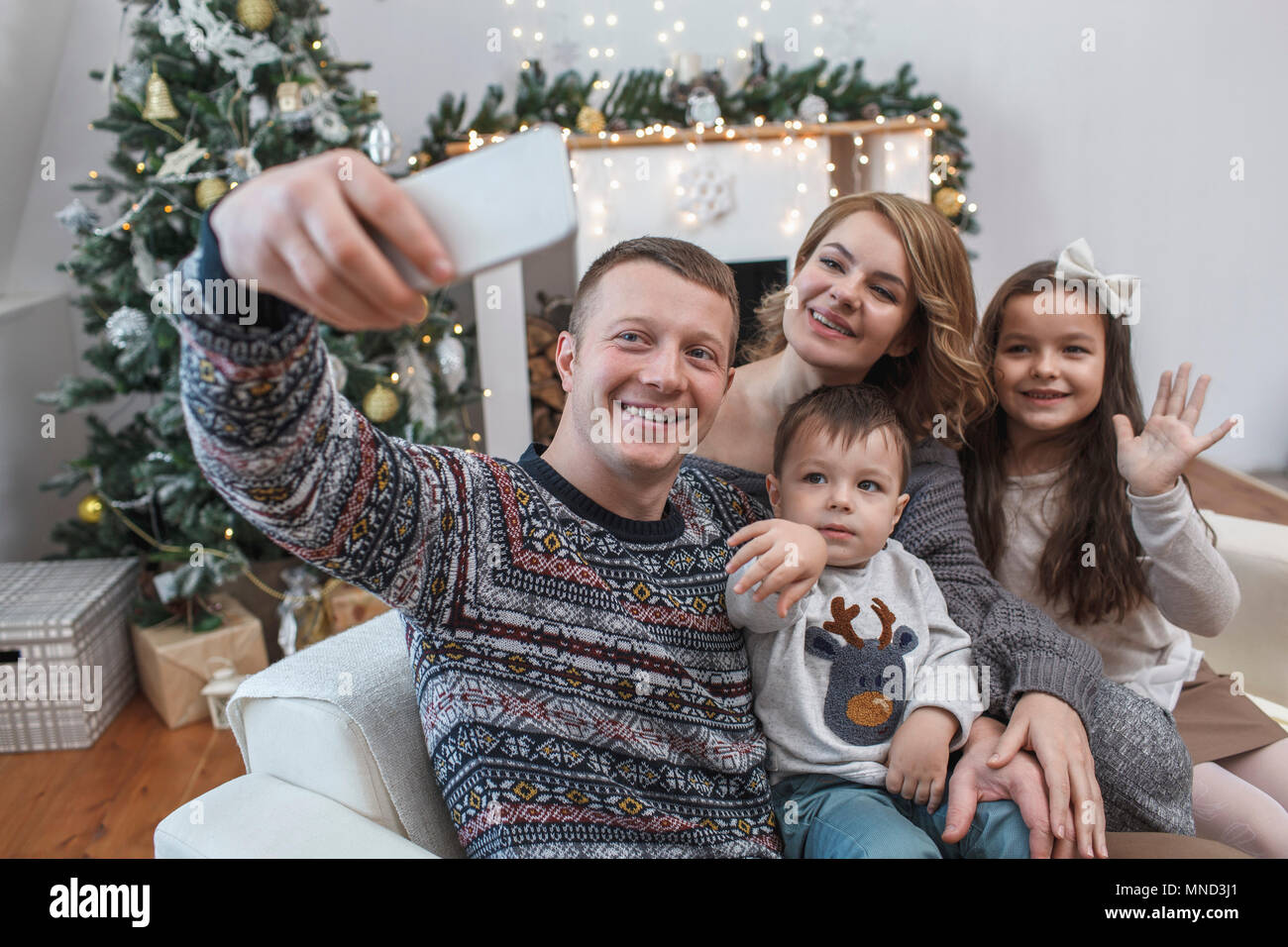 Happy man taking selfie with family on sofa at home during Christmas Stock Photo
