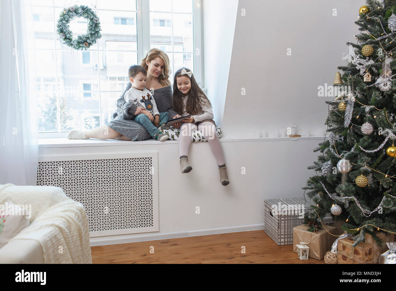 Woman sitting with children on window sill at home during Christmas Stock Photo