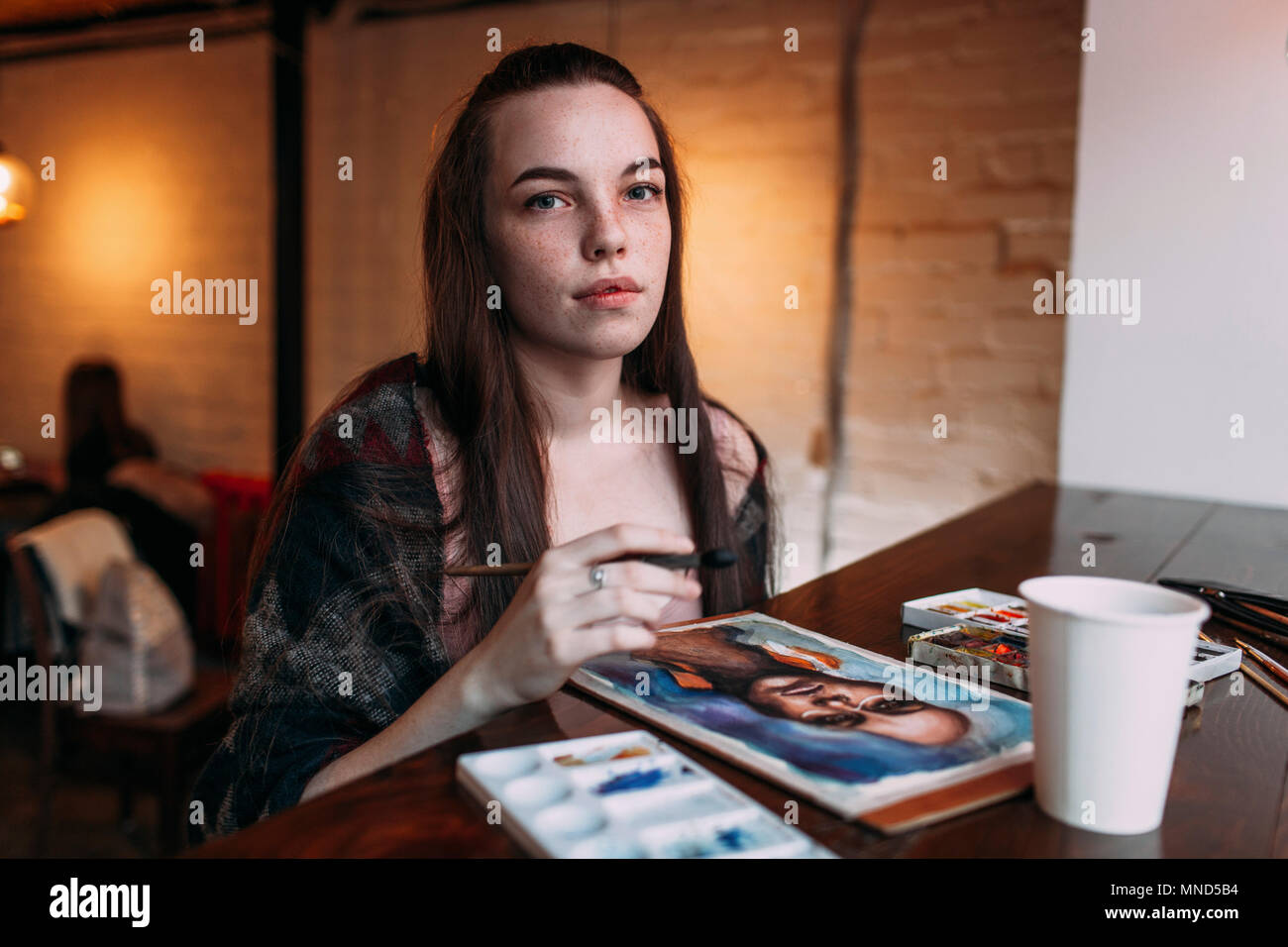 Portrait of beautiful young woman sitting by painting on table at cafe Stock Photo