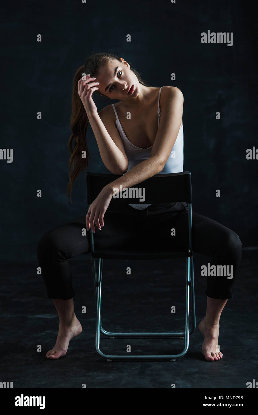 Full length portrait of young fashion model sitting on chair against black background Stock Photo