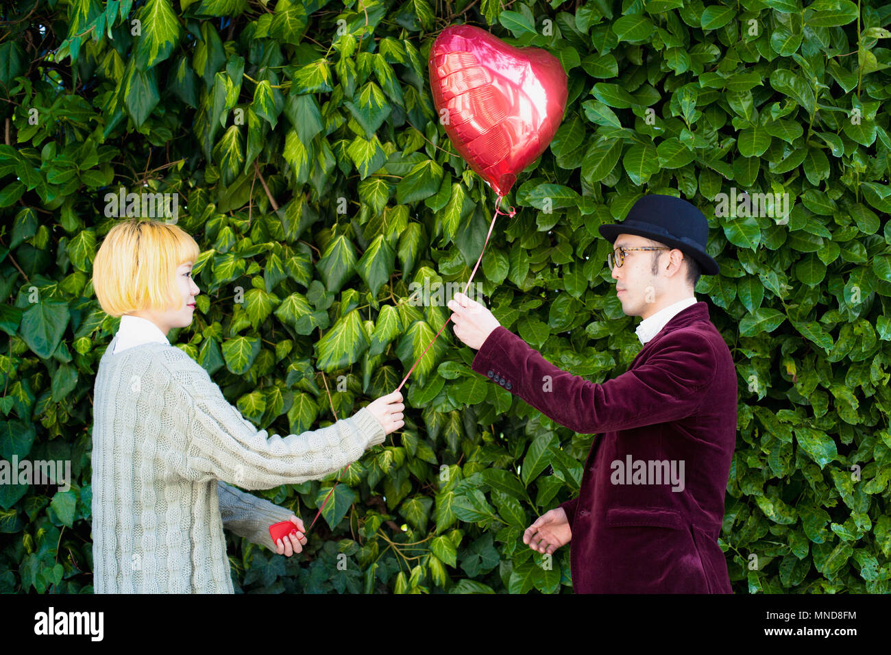 Side view of young couple holding heart shape balloon against plants at ...