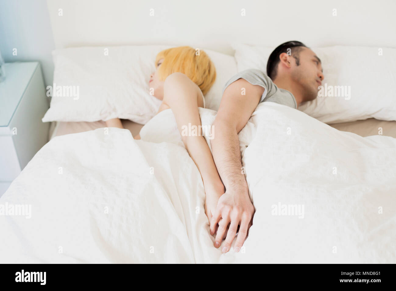 High angle view of couple holding hands while sleeping back to back in ...