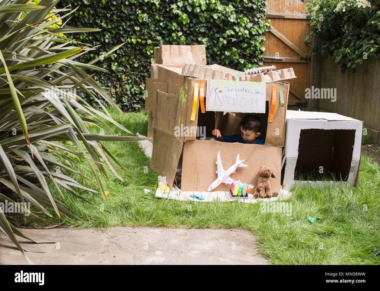 Boy in cardboard playhouse with toys at back yard Stock Photo