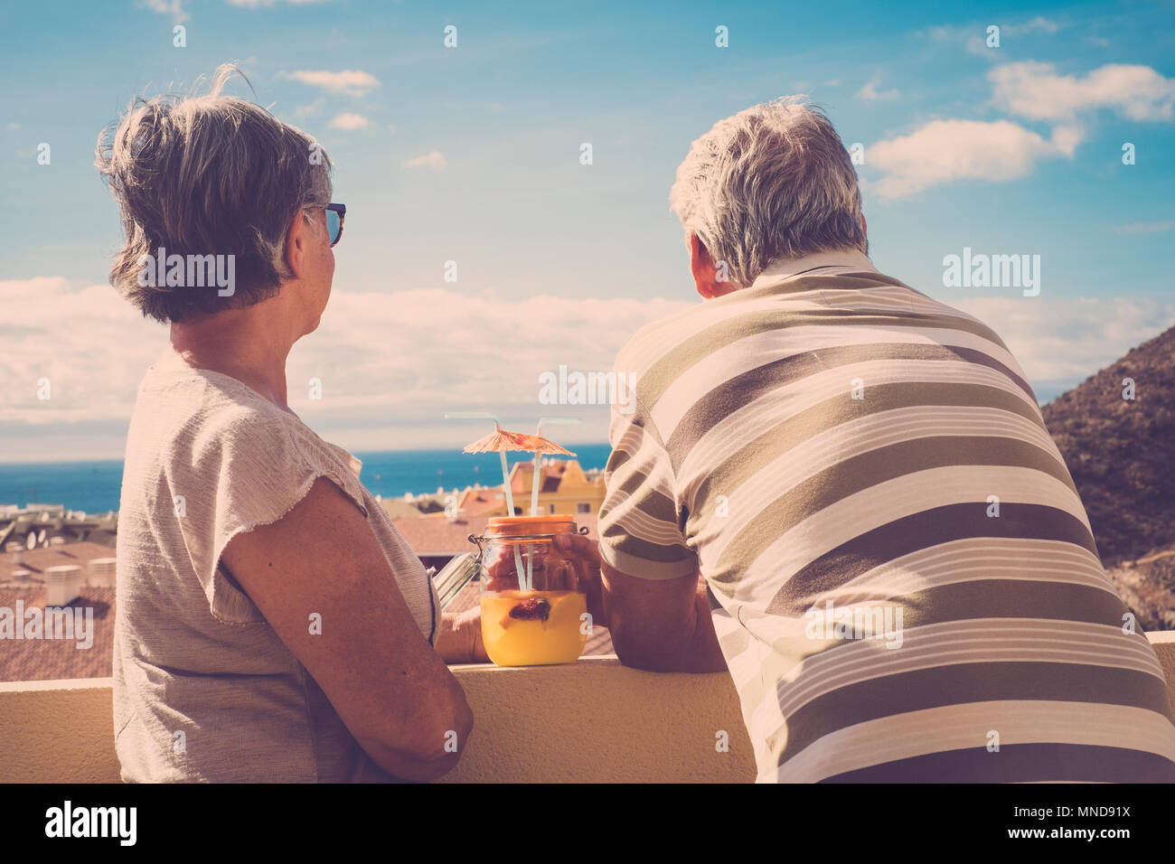 two elderly man and woman looking together the ocean view in vacation. Back view with roofs in vintage style. Stock Photo